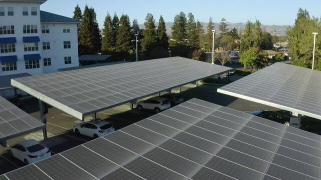 Aerial view around solar carport shelter panels, near apartments, during golden hour - orbit, drone shot