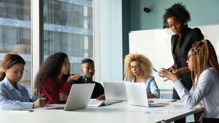 Concentrated multiracial colleagues sit at table in boardroom discuss company financial paperwork in group together. Diverse multiethnic businesspeople brainstorm cooperate at team briefing in office.
