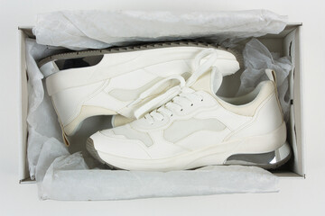 White women's sneakers in a box with paper.