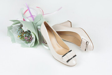 Bright beige shoes on a white background with a bouquet of flowers.