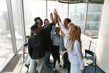 Overjoyed multiracial businesspeople give high five at meeting in office celebrate shared business...