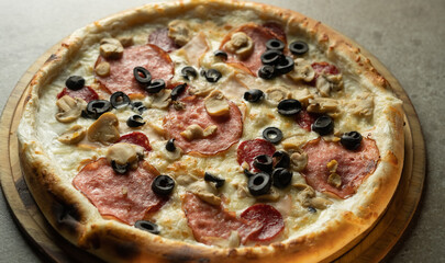 Hot pizza with olives, cheese and sausage on a wooden board on a gray background. Ready-made pastries in a pizzeria.