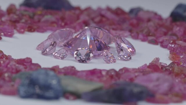 pink sapphires diamonds of various sizes are centered on a white background, surrounded by uncut raw red garnet stones..