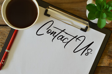 Top view of plant, a cup of coffee, pen and white paper witten with text CONTACT US. Business...