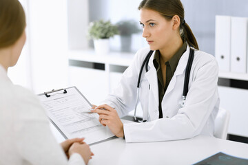 Woman-doctor and patient sitting and talking at hospital office. Green color blouse suits to therapist. Medicine and healthcare concept