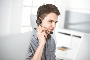 Casual dressed young man using headset and computer while talking with customers online. Call center, business concept