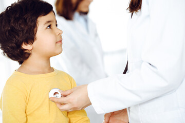 Woman-doctor examining a child patient by stethoscope. Cute arab boy at physician appointment. Medicine help concept