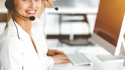 Blond female customer service representative is consulting clients online using headset in sunny office. Call center concept