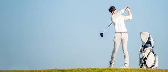 Poster Asian man golfer standing  on slope  with golf bag hitting  golf ball on blue sky background  at golf course © Tawan