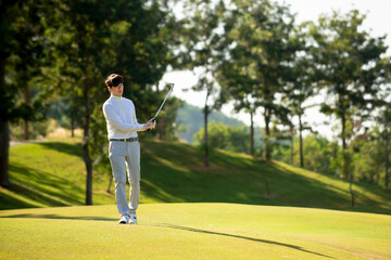 Asian man golfer  holding golf club walking  on fairway at golf course