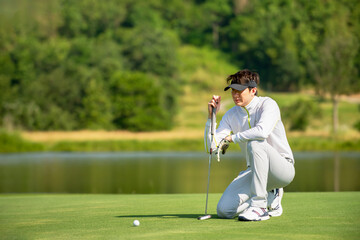 Asian man golfer  sitting  on fairway aiming ball to  golf hold at golf course