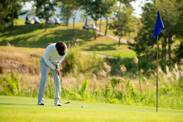 Asian man golfer  holding golf club hitting ball to golf hold  on fairway at golf course