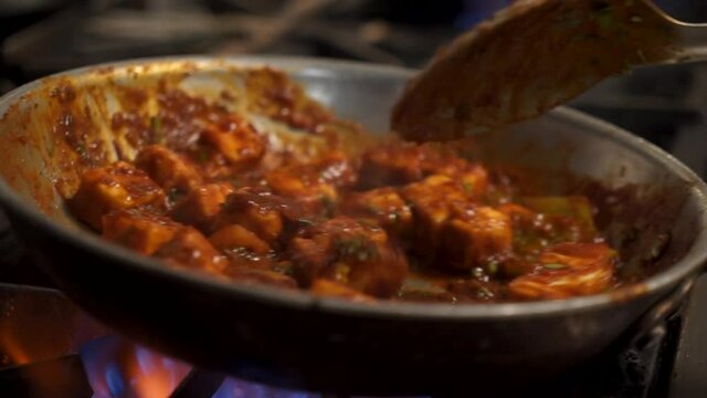 Chef tosses traditional paneer tikka masala over flame, close up slow motion 4K