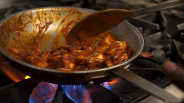 Paneer tikka masala tossed in pan over fire in restaurant kitchen, close up slow motion 4K