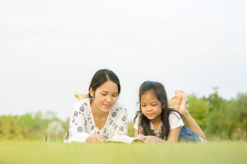 Fototapeta premium Beauty smiling mother and little sons reading book outdoor on green grass field
