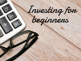 Top view calculator and eye glasses with text Investing for beginners written on wooden background.Business concept.
