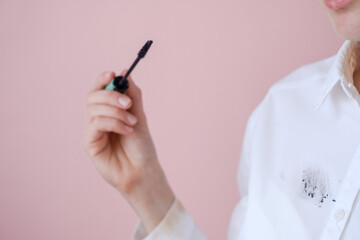 cosmetic stain on white shirt. In the female hand mascara. isolated on pink background