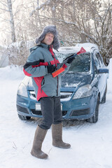 Cheerful, cheerful, A man in huge felt boots and a fur hat stands by a car with a snow brush....