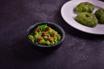 Green pkhali with pomegranate seeds on a dark stone table.