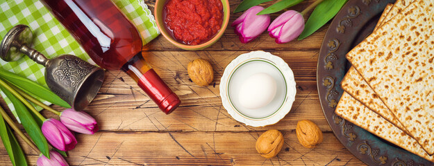 Jewish holiday Passover background with matzah, seder plate, wine and tulip flowers on wooden table.