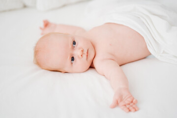 cute red-haired baby lies on a white bed. concept of baby care