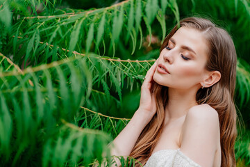 portrait. beautiful woman with light eyes in white dress against of green leaves