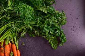 A bunch of carrots with tops on a dark stone table.