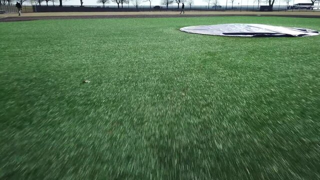 Drone flying forward at low altitude across green baseball field from batter's box in Bridgeport, Connecticut, USA.