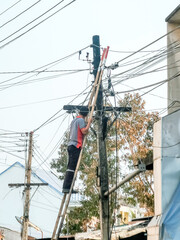Asian electrician on a ladder repairing wire of the power line on electric power pole in the...