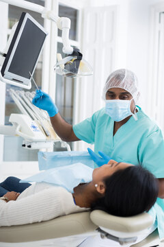 Qualified hispanic dentist pointing at teeth x-ray image on computer monitor explaining future treatment to female patient in dental clinic