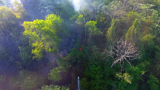 Aerial drone view of a firetruck spraying water on smoking, glowing forest fire