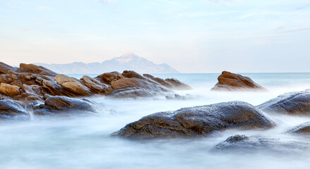 Scenic sunset at Sarti beach, Halkidiki, Sithonia, Greece, Europe; view of the fantastic rocky shore with the Mt. Athos in the background; dramatic seascape of the Aegean sea; long exposure shot
