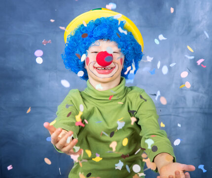 yyoung child dressed as a clown with wig and fake nose has fun playing with colorful confetti celebrating carnival