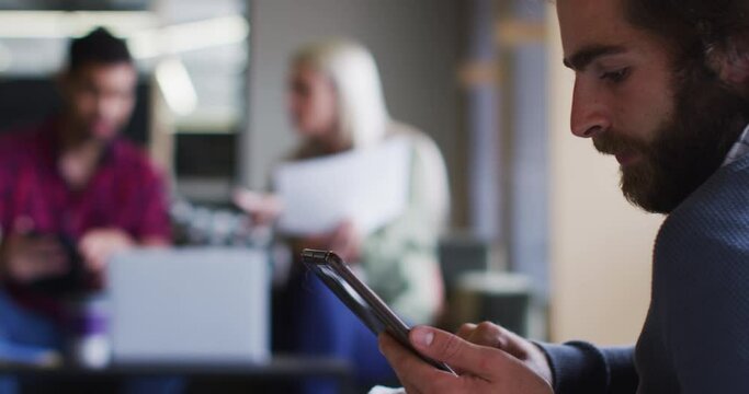 Diverse business people sitting using digital tablet and goign through paperwork in modern office