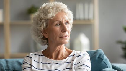 Fototapeta na wymiar Head shot close up pensive old senior hoary woman looking in distance, recollecting memories or feeling lonely at home. Lost in thoughts middle aged grandmother relaxing on sofa, missing or mourning.