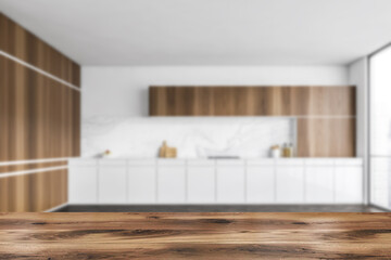 Fototapeta na wymiar Wooden desk on foreground, blurred white and wooden empty kitchen set