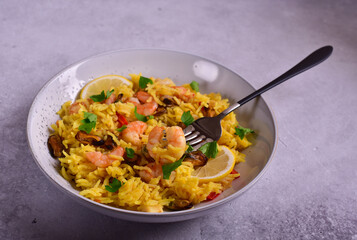 Paella with shrimps, parsley and lemon on a grey stone table.