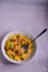 Paella with shrimps, mussels, lemon, herbs in a gray plate on a gray stone background.