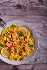 Paella with shrimps, mussels, lemon, herbs in a gray plate on a wooden table.