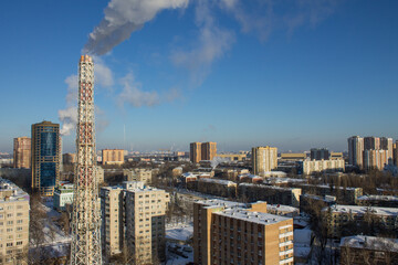 heating system pipe with steam and urban landscape with modern residential buildings against the background of blue clear sky on a frosty winter day in Reutov Moscow region Russia