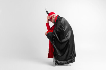 Caucasian male model in halloween black red costume and sunglasses with hat and horns posing over...