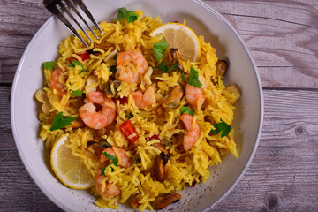 Paella with shrimps, mussels, lemon, herbs in a gray plate on a wooden table.