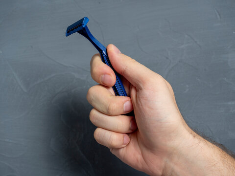 Close Up Of A Man's Hand Holding A Blue Plastic Razor On A Gray Textured Background