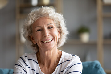 Fototapeta na wymiar Head shot close up portrait of happy grey-haired old retired woman sitting on sofa. Sincere smiling middle aged grandmother enjoying video call conversation with friends or grown children, screen view