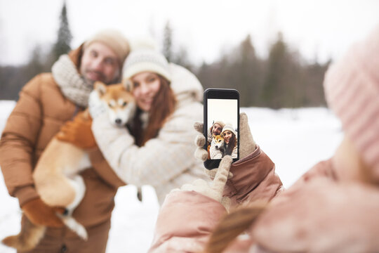 Close up of teenage girl taking photo of parents while enjoying walk outdoors together in winter forest, focus on smartphone screen, copy space