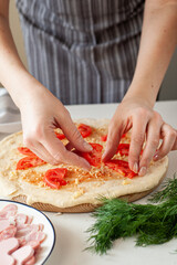 The process of making homemade pizza for Valentine's Day. Women's hands lay the ingredients cut in the form of hearts on the base of the dough.