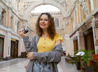 Cheerful curly hair woman tourist with retro camera in city. Travel concept