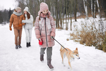 Full length portrait of cheerful teenage girl walking dog on leash outdoors in winter while enjoying nature with family, copy space