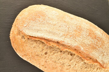 One flavorful loaf without yeast with bran flakes on a slate board, close-up.