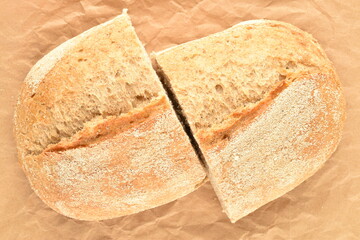 Two halves of a fragrant loaf without yeast with bran flakes, close-up, on brown paper.
